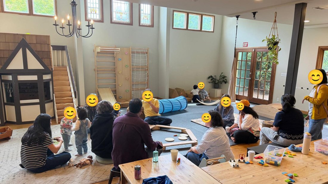 The room on the day. Parents and toddlers sitting together on rugs in the middle, a climbing wall, slide and play house along one wall, and low tables with blocks around the edge.